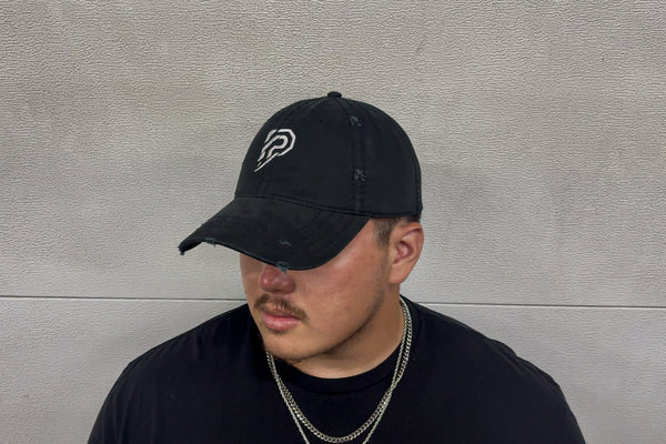 Person wearing a black cap with a logo against a gray wall
